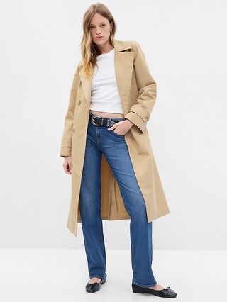 woman wearing a white t-shirt, jeans and a tan trench coat. 
