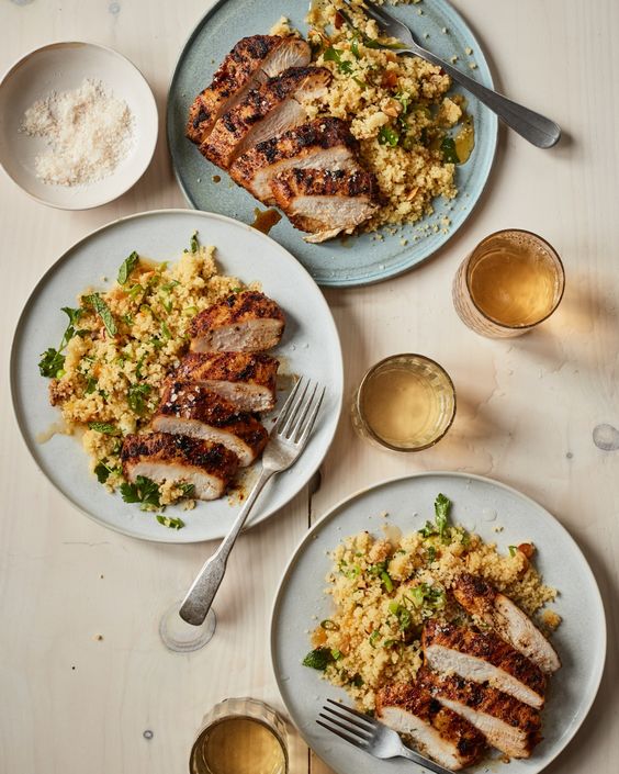 Grilled Moroccan Chicken on 2 plates with couscous and glasses of wine. 