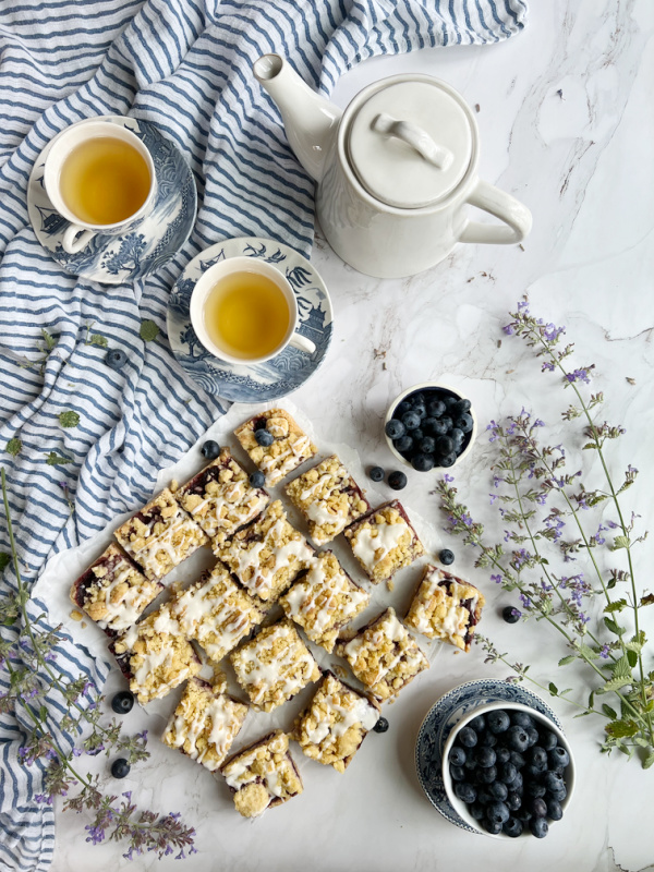 blueberry crumb bars with glaze and 2 cups of tea and a teapot. 
