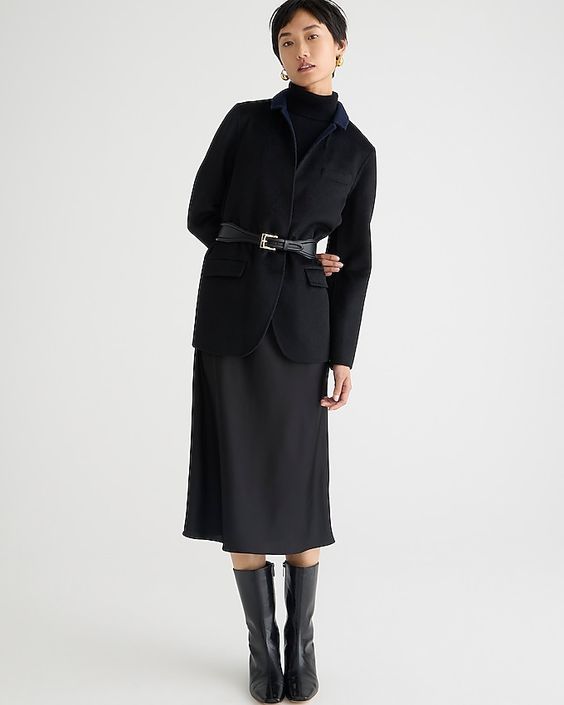 A woman wearing a black skirt, sweater, belt and boots. 