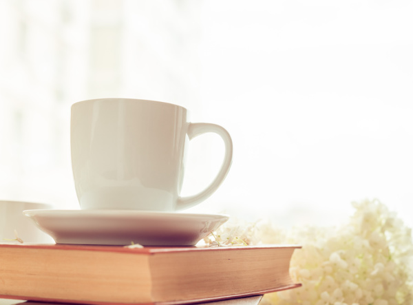 A white cup on a book with white hydrangeas in the background.