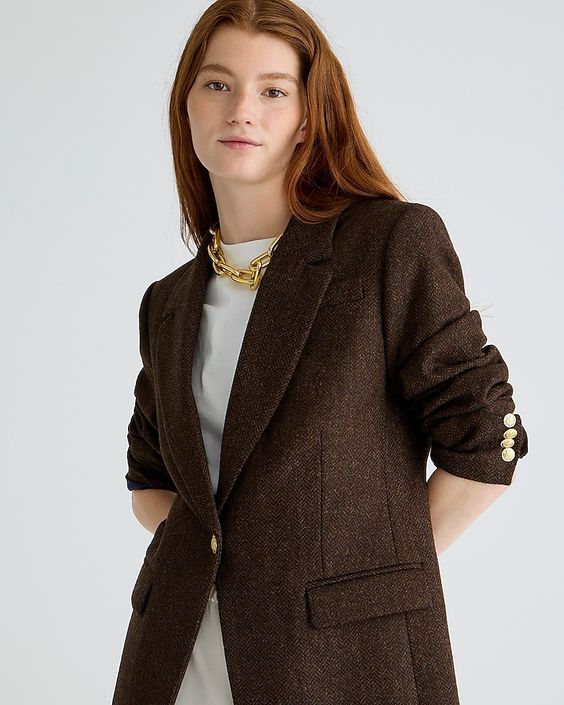 Woman wearing a white t-shirt and a brown herringbone blazer with gold jewelry. 