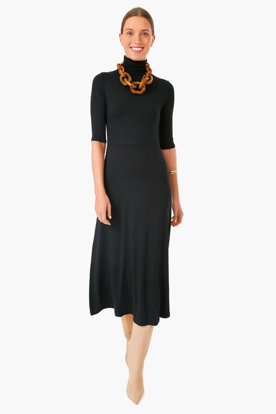 Woman wearing a black turtleneck dress with a large tortoise shell chain necklace. 