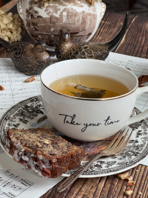 A cup that says take your time filled with tea and a piece of chai spiced bread.