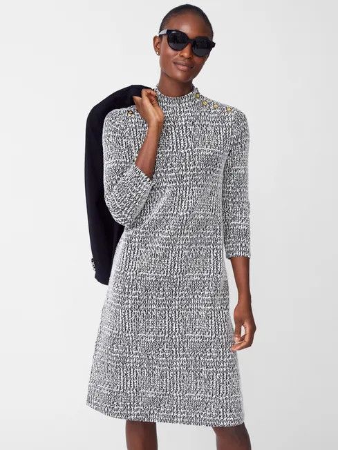 Woman wear and black and white houndstooth dress with a black jacket slung over one shoulder. 