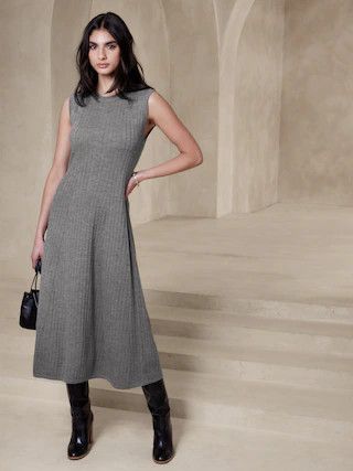 Woman wearing a sleeveless gray sweater dress, black boots and a black bag. 