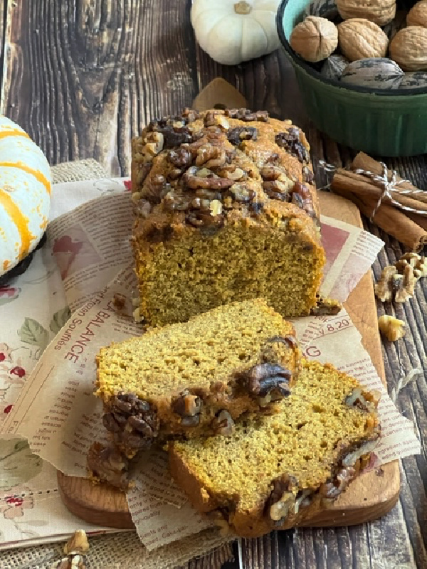 pumpkin bread with walnuts sliced on a wood cutting board. 