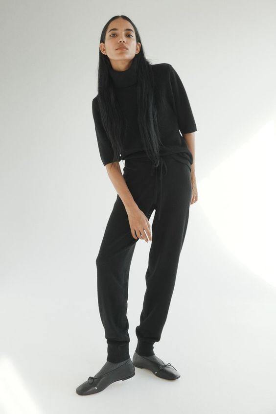 Woman wearing a black sweater and joggers with black shoes.