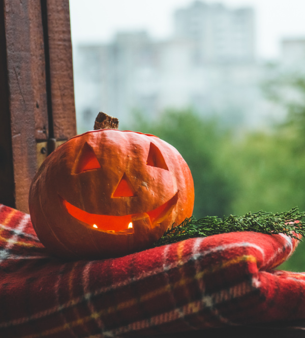 carved pumpkin sitting on a plaid blanket in a window.