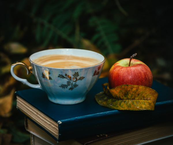 a teacup on top of a book next to an apple.