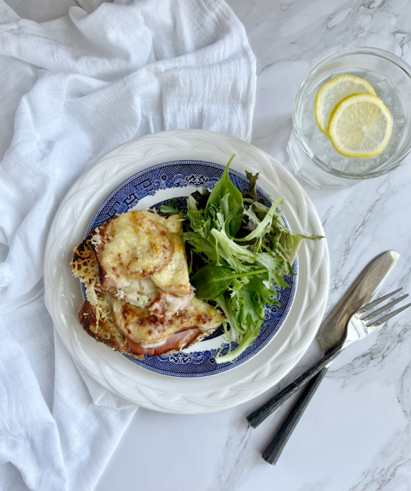 ham, gruyere, pickled apple tartine on blue and white transfere-ware plates and a glass of water with a slice of lemon. 