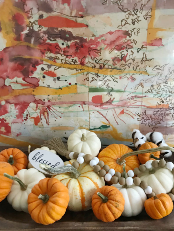 white and orange pumpkins in a wood bowl with an abstract piece of art