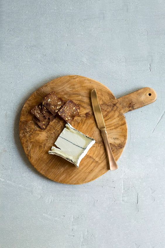 Round wood cutting board with a cheese knife and a wedge of cheese.