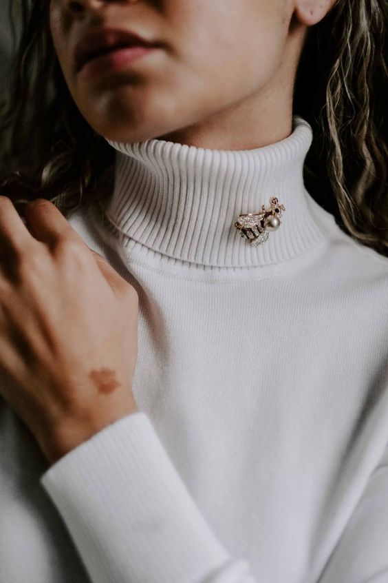 A woman wearing a tan turtleneck with a bee brooch. 
