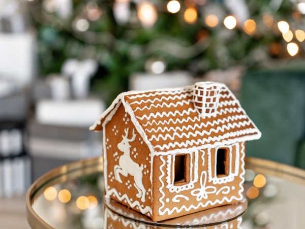 gingerbread house on a mirrored table with a chrsotmas tree in the background.