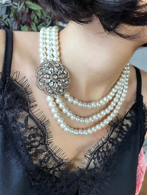 woman wearing a black slip dress with 3 strands of pearls and a vintage brooch.
