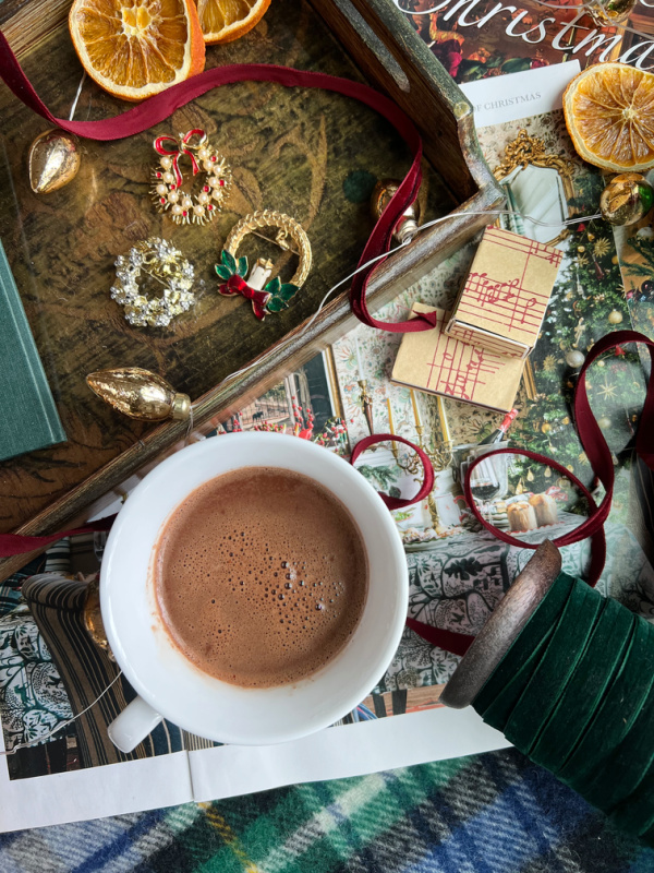 December Flatlay with hot chocolate, dried oranges, wreath brooches on a tray and magazines.