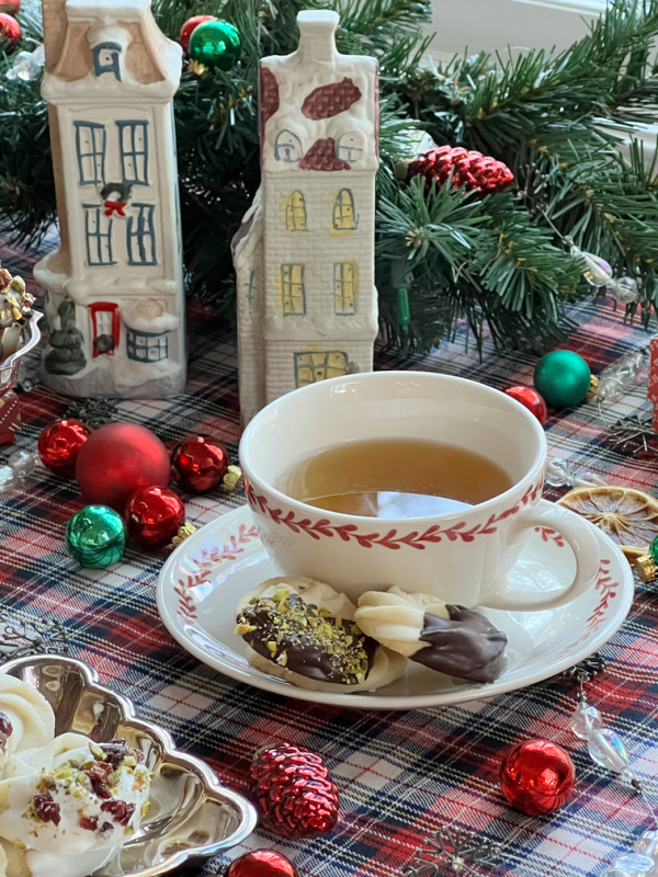 cup of tea and viennese whirl cookies with christmas decorations including 2 victorian houses and ornaments.