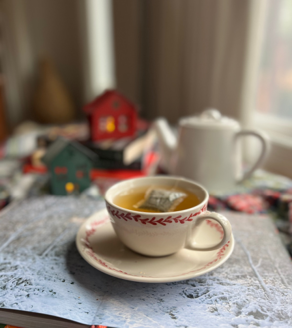 White and red cup of tea, white teapot and a pile of books.