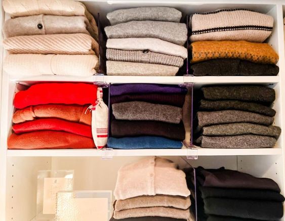 A well organized closet with stacks of sweaters folded. 