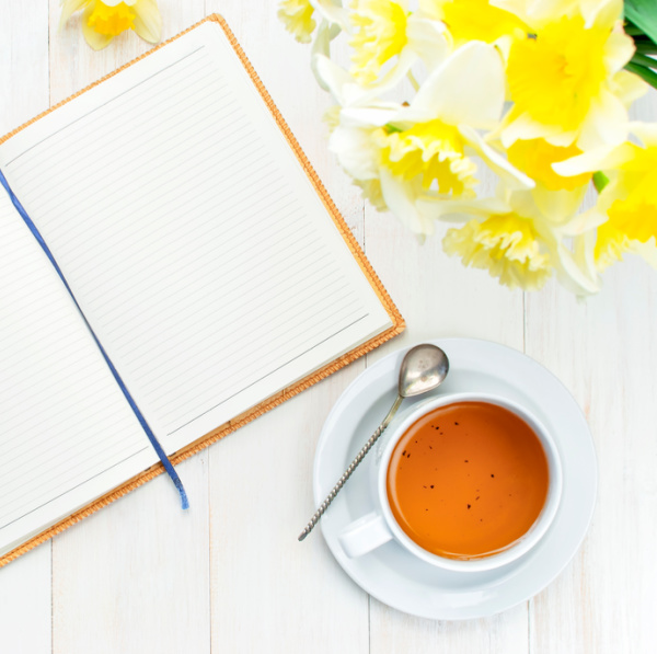 Yellow daffodils and a cup of tea with an open journal.