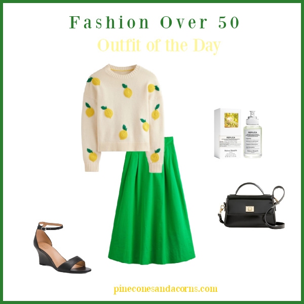 Fashion over 50 White sweater with lemons and a green skirt, black shoes and black handbag.