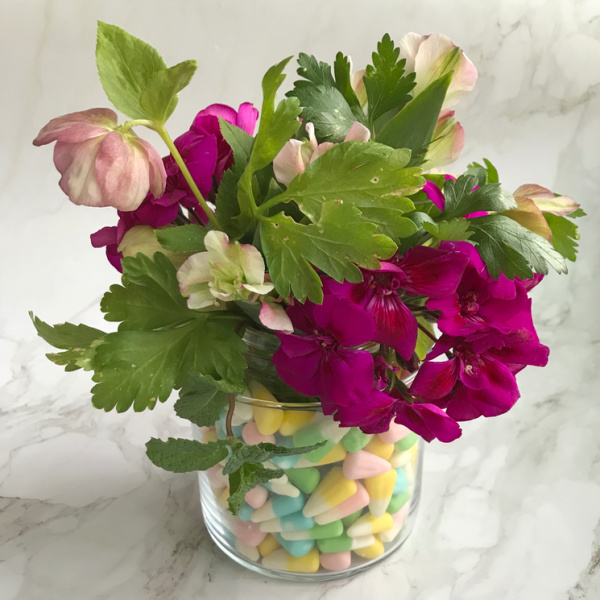 Easy-Easter-Flower-Arrangement with geraniums, herbs and lenten roses in a clear glass vase with pastel candy corn.