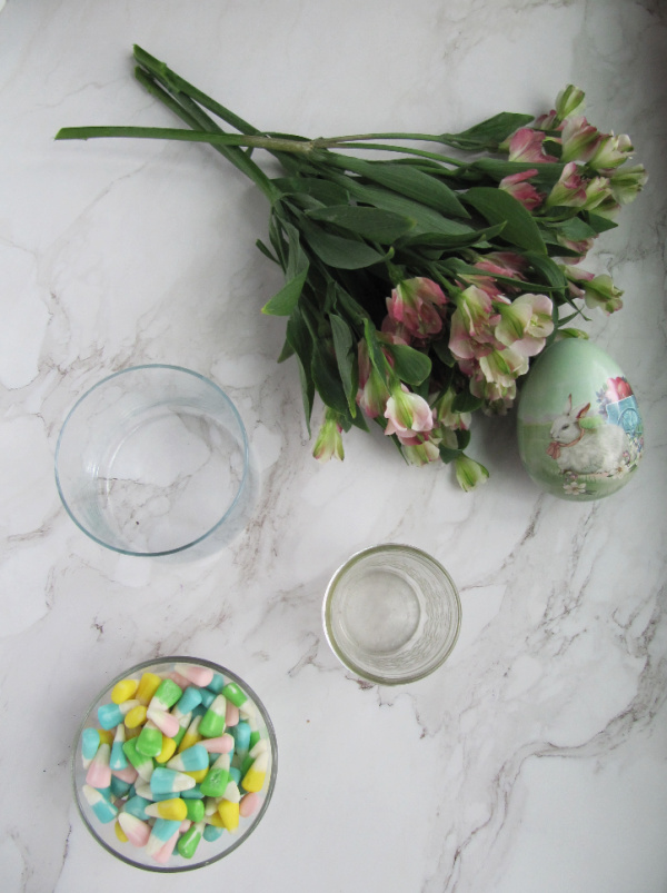 flowers, an easter egg, a bowl of easter candy and two clear glass vases. 