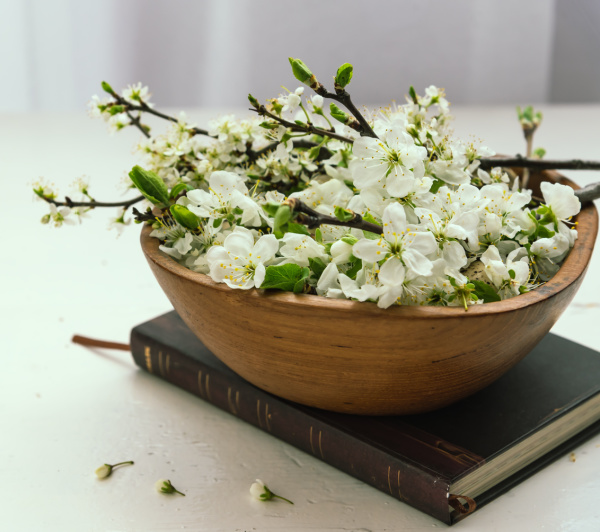 pear blossoms in a wood bowl sitting atop a black book