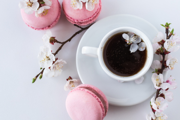 Pink macarons and a white cup and saucer with pink cherry blossoms.