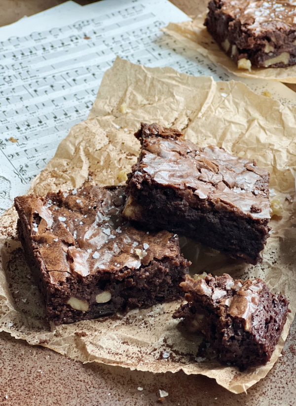 Two chocolate brownies on brown parchment paper. 
