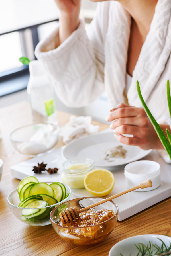 Spring self-care ideas, a woman in a white robe using natural skin care including cucumbers, honey, lemon and salt. 