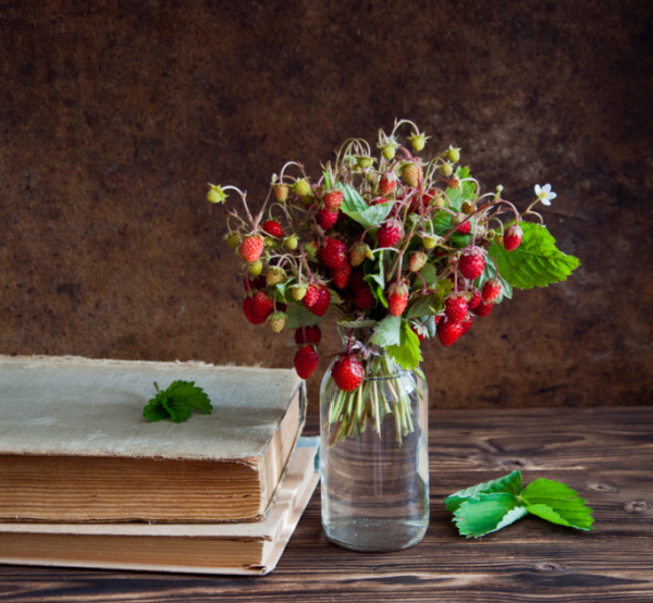strawberries in a clear glass vase sitting next to a book