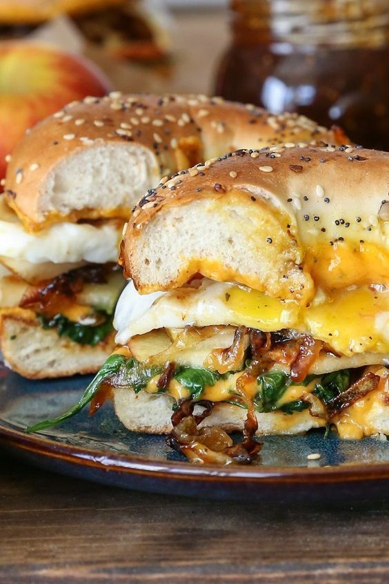 grilled cheese bagel breakfast sandwich with sliced apple, pear, cheddar cheese, caramelized onions, arugula, and sunny-side up egg.