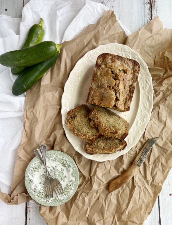 sliced zucchini bread on a white platter with a pile of zucchini.