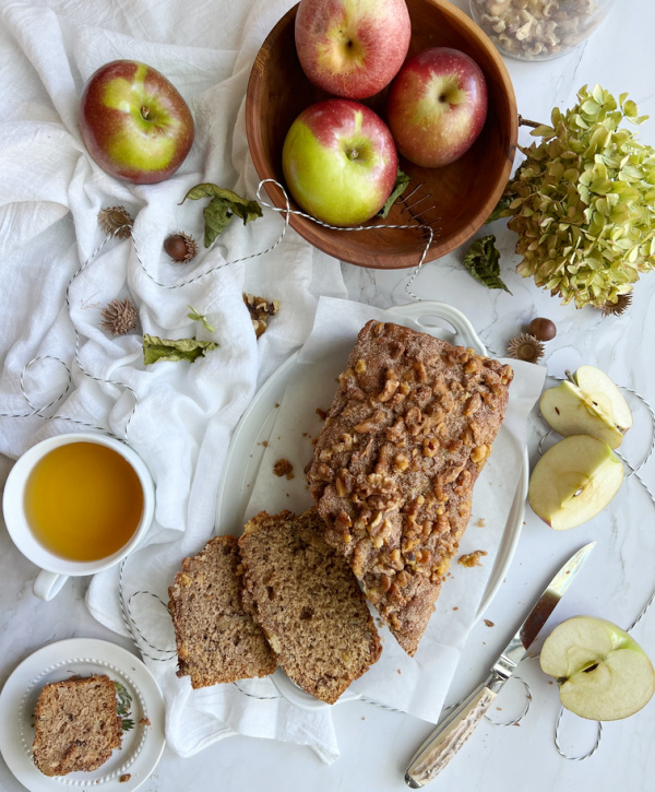 Applesauce bread with a wood bowl of apples and sliced apples and a cup of tea. 
