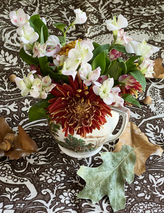 Fall flowers in brown transferware jug in brown and white fabric with animals.