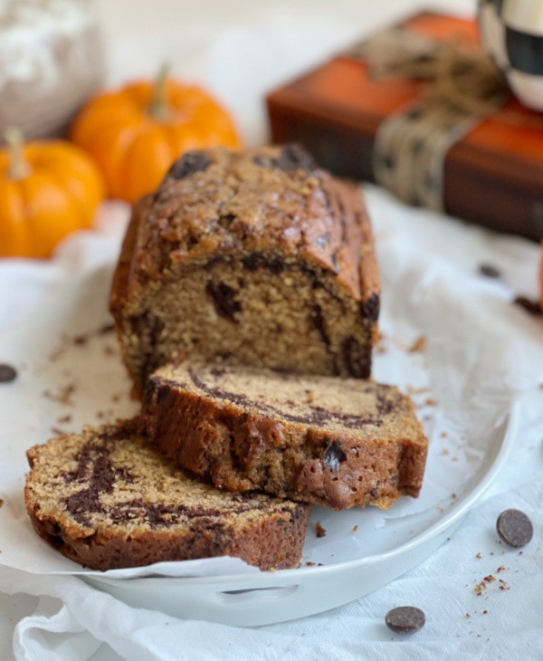 pumpkin bread on a white plate with orange pumpkins and an orange and black book. 