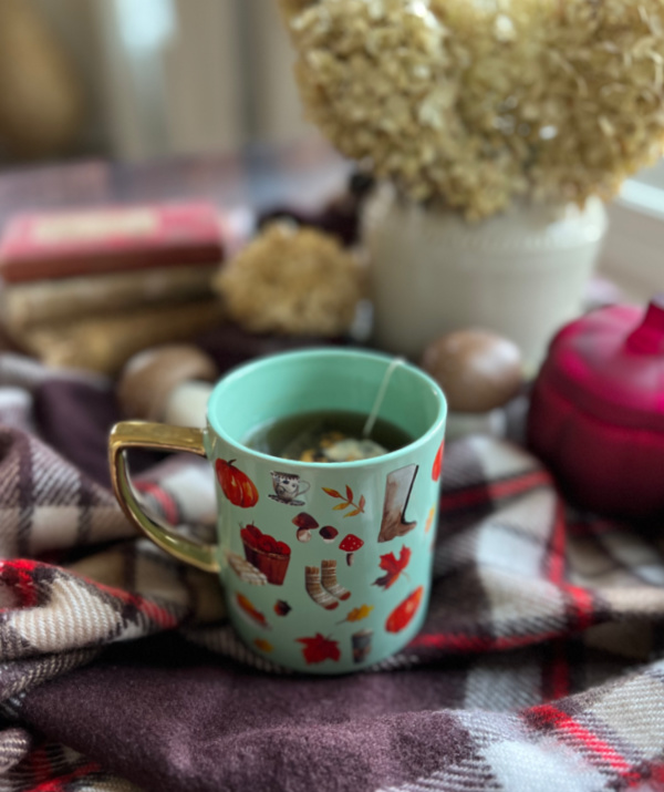 Fall vignette with mug of tea and a pumpkin candle on a plaid throw
