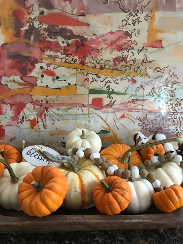 dough bowl full of orange and white pumpkins sitting in front of a piece of abstract art