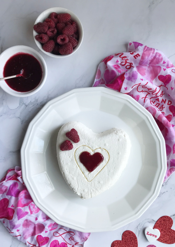 Coeur a La Creme With Raspberry Sauce on white plate with raspberries and small heart cutout. 