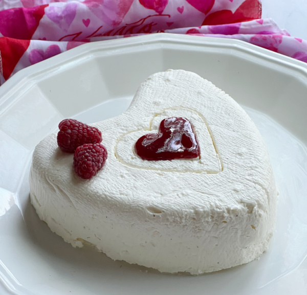 Coeur a La Creme With Raspberry Sauce on white plate with raspberries and small heart cutout. 