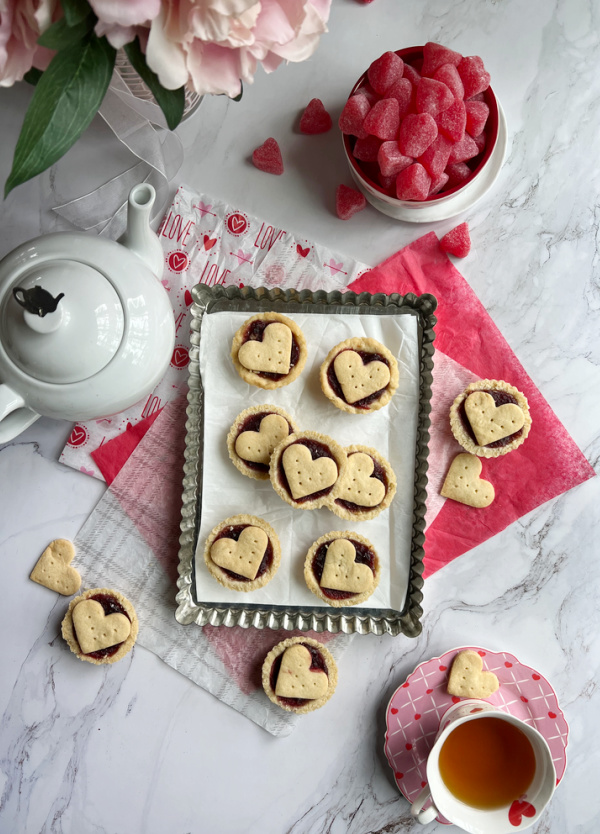 Raspberry almond tarts with a pot of tea and a vase or peony flowers.