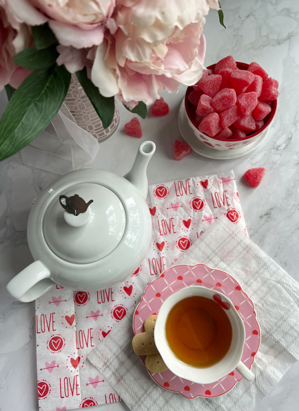 Valentine Flatlay pot of tea bowl of heart candy and a vase of peonies.