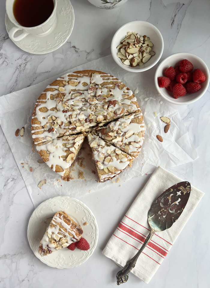 Raspberry Almond Frangipane Coffee Cake with a small white bowl of raspberries and almond slices as well as a cup of coffee. 
