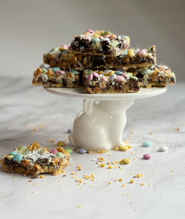 Easter Magic Bars piled on a white cake plate with a bunny base.