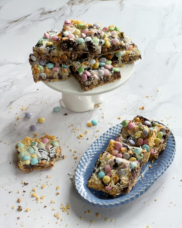 White cake plate and a blue oval platter with Easter Magic Bars topped with M&M.