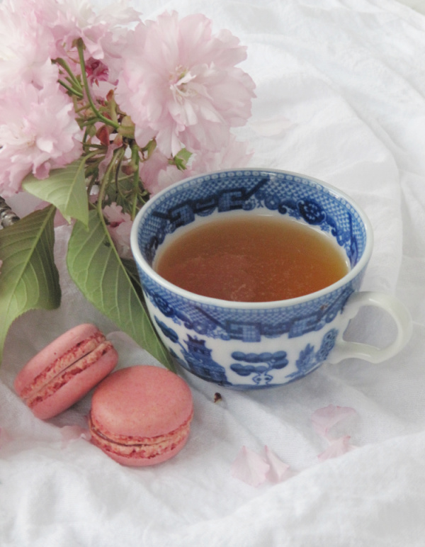 cherry blossoms and a cup of tea with 2 pink macarons cookies.