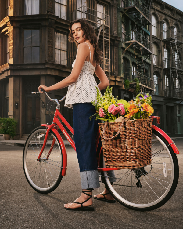 Girl straddling a red bike with a basket of flowers, Kate Spade NY x Target. 