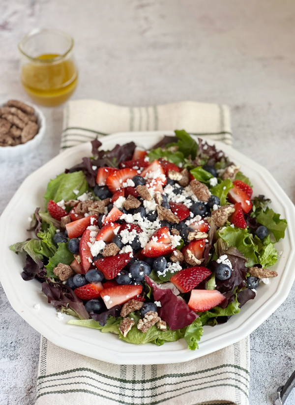strawberry salad with candied pecans and blueberries on a white plate.
